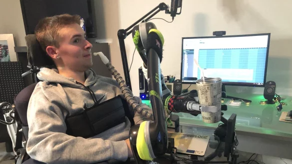 Rayk Br&auml;tzkus sitzt in seinem Wohnzimmer in Lockhausen. An seinem Rollstuhl ist ein Greifarm befestigt, den er &uuml;ber einen Joystick steuert. Auf seinem Rechner hat er ein Musikprogramm, mit dem er Rap-Musik macht.&nbsp; - &copy; Sven Kienscherf