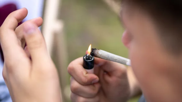Ein junger Mann zündet sich einen Joint an – die Debatte um die Cannabis-Legalisierung in Deutschland spitzt sich wieder zu. - © picture alliance/dpa