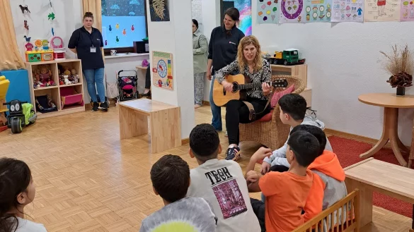 Janine Dahlmann spielt die Melodie auf der Gitarre und ermuntert die Kinder in der Notunterkunft in H&ouml;rste zum Mitsingen. - &copy; Fotorechte: Malteser