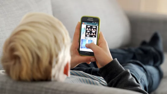 Ein Kind liegt auf einem Sofa und blickt auf sein Smartphone. - &copy; Tobias Hase/dpa
