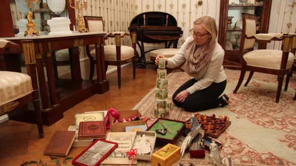 Lisa-Marie Bergann, Ausstellungskuratorin im Residenzschloss, richtet die Geschenke-Ecke im Wohnzimmer her. Dort sind allerlei Spiele, Bücher und andere Präsente zu finden - alles Originale aus dem Fürstenhaus. - © Jana Beckmann