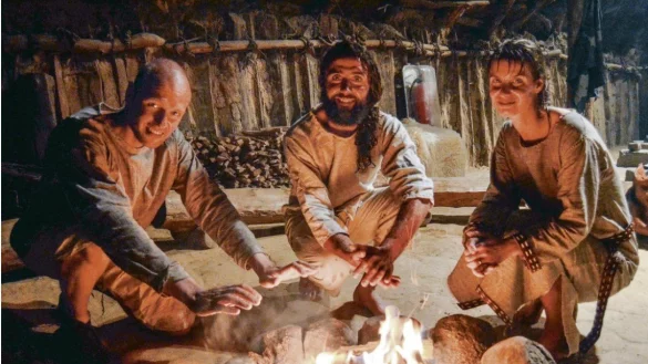 Die Wärme tut gut: Schnell haben die Ötzi-Walker, Marco Hocke (v.l.), Lukas Heinen und Veronika Hocke mit Feuerstein ein Feuer entzündet im jungsteinzeitlichen Landhaus des Archäologischen Freilichtmuseums und wärmen sich daran die kalten Glieder. Auch feuchte Schuhe, Kleidung und Felle werden zum Trocknen in die Nähe des Feuers gelegt. - © Sibylle Kemna