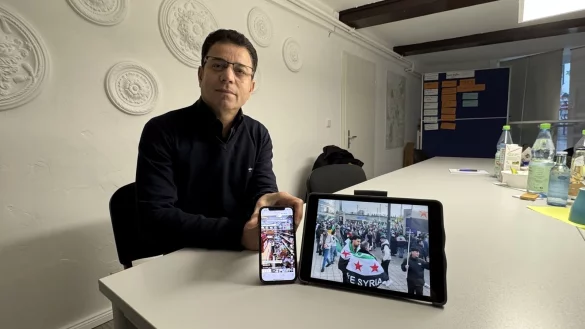 Perwer Shamoo zeigt zwei Bilder: rechts feiernde Syrer in Deutschland, die sich über den Sturz Assads freuen und ein Bild, auf dem durch die Islamisten zerstörte Alkoholflaschen zu sehen sind. - © Sven Kienscherf