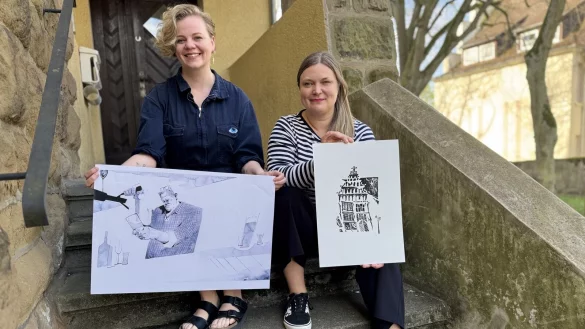 Kuratorin Celia Kaspar (links) und Stadtarchivarin Sonja Beinlich planen eine Kunstausstellung. Die Bilder, die sie auf der Treppe der "Gelben Schule" in den Händen halten, zeigen Werke von Kaspar. Links ist der Wirt der Salzufler Kneipe "Lebenslang", Jupp Westfeld, zu sehen. - © Sven Kienscherf