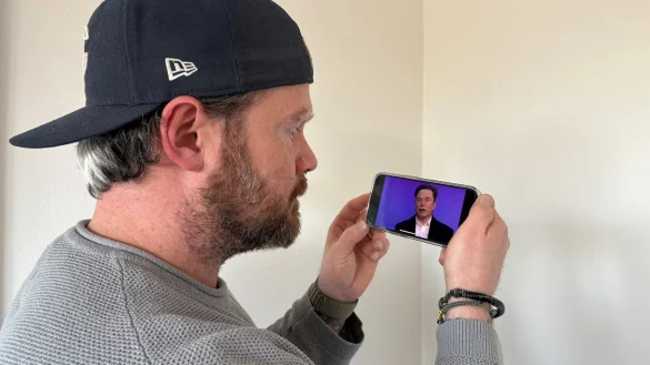 Kriminalhauptkommissar Thomas Konrad sieht sich auf seinem Handy das Motiv aus einem Deepfake-Video mit dem Antlitz von Elon Musk an. Das komplett künstlich animierte Gesicht des Tech-Milliardärs sieht dem "Original" sehr ähnlich. - © Jan Schillmann