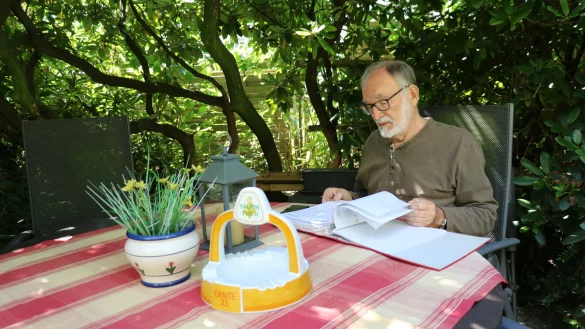 Friedrich-Wilhelm Biermann blättert durch einen Ordner. Im Hintergrund ist der Zaun zu erkennen, hinter dem sich der Hahn zunächst aufhielt. - © Alexandra Schaller