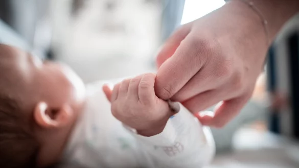 Ein Baby h&auml;lt sich an der Hand einer Erwachsenen fest - &copy; Foto: Fabian Strauch/dpa/Archivbild