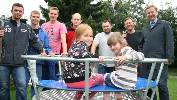 Bald geht es rund: Karina und Jolina (vorne von links) freuen sich, dass sich Daniel Hobusch, Daniel Giesbrecht, David Gossen, Markus Friesen, Albert Bartsch, Jurij Muss sowie B&uuml;rgermeister Dr. Andreas J. Wulf (von links) f&uuml;r den neuen Spielplatz einsetzen. - &copy; Sandra Castrup