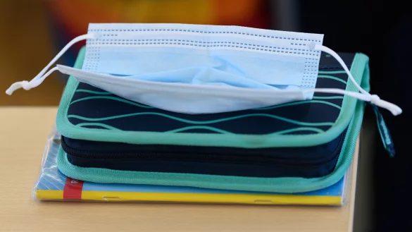 Eine medizinische Maske liegt auf einer Schulmappe in einem Klassenzimmer.  - © Robert Michael/dpa-Zentralbild/dpa