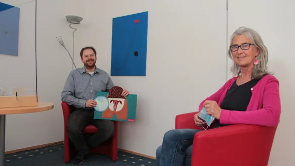 S&ouml;ren R&uuml;tten &ndash; mit einem Modell einer Geb&auml;rmutter in der Hand &ndash; und Dorothee Brand beraten auch in Corona-Zeiten. Mit Trennscheibe und L&uuml;fter im Beratungsraum.&nbsp; - &copy; Carolin Brokmann-F&ouml;rster