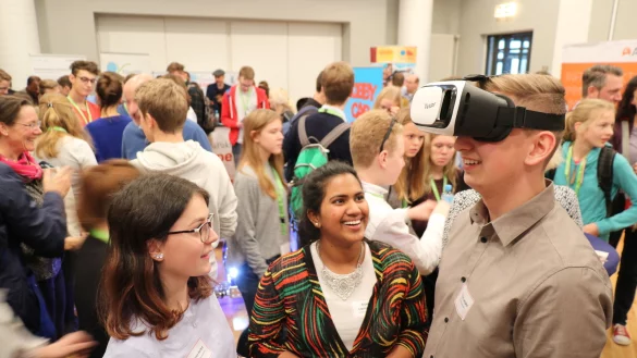 Beim Klimagipfel: Schülermoderator Florian Lempke testet die VR-Brille, die vom Unternehmen Dachser und dem Kinderhilfswerk „Terre des Hommes" zur Verfügung gestellt wird. Darin kann ein Blick auf die Lage in Sambia geworfen werden. Ihn begleiten seine Moderationspartnerinnen Maren Herbst (links) und Anjana Logeswaran. - © Alexandra Schaller