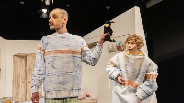 August (Jan-Niklas Shadan Mavigök) hält "Peter the pengiun" während des Durcheinanders der chaotischen, aber liebevollen Aufräum-Debatte hoch. Judy (Magdalena Weiß) ist gespannt, was als nächstes geschieht. - © Landestheater Detmold/ Jochen Quast
