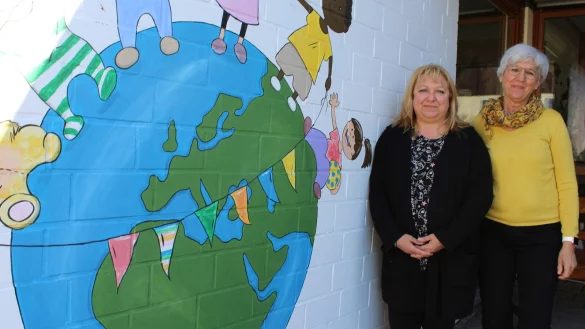 Leiterin Silke Schmidt (links) und Kollegin Carmen Skupin stehen vor einem Bild, das den Eingangsbereich der Kita ziert. Es spiegelt das Motto der Einrichtung wider: Alle sind gleich. - © Lorraine Brinkmann