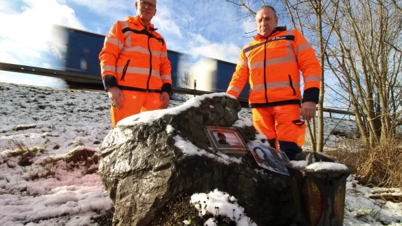 Ralf Kowalleck (rechts) und Andreas Stratmann stehen an einem Stein, der an einen Kollegen der beiden Straßenmeister erinnern soll. 2001 verstarb er wenige Meter hinter den beiden auf der A44, als ihn ein Auto in einem abgesperrten Bereich erfasste. - © Lukas Brekenkamp