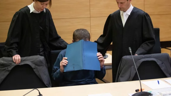 Der Angeklagte im Pausenbrot-Prozess sitzt mit einer Mappe vor dem Gesicht im Gerichtssaal neben seinen Verteidigern, Christina Peterhanwahr und Henning Jansen. - &copy; picture alliance