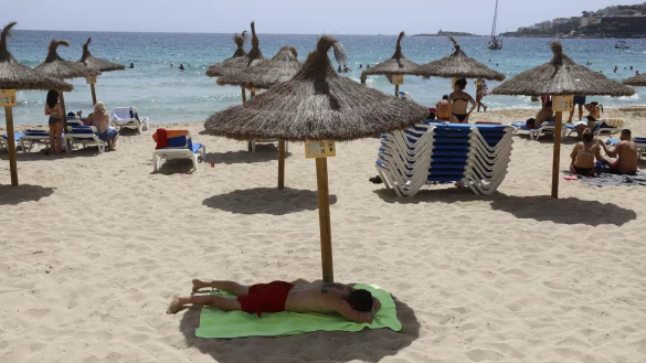 Ein Mann liegt im August unter einem Sonnenschirm am Strand von Cala Major. Die pauschale Reisewarnung f&uuml;r fast alle gut 160 L&auml;nder au&szlig;erhalb der EU und des grenzkontrollfreien Schengen-Raums wird am 30. September enden. Danach gelten individuelle Bestimmungen. - &copy; Clara Margais/dpa