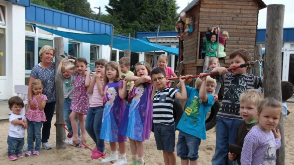 Leiterin Claudia Haustein (links im Bild) stellt sich mit einigen Kindern der Kita „Schatztruhe" auf dem Spielplatz zum Jubiläumsfoto auf.  - © Marlen Grote
