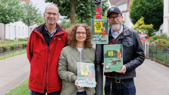 Auch am Wall erinnert ein neues Schild jetzt freundlich daran, dass es sich ohne die Hinterlassenschaften der Vierbeiner einfach schöner in Detmold spazieren gehen lässt. (von links) Stephan Szymanowski und Inga Müller aus dem Team Freiraumplanung der Stadt Detmold und den Detmolder Cartoonisten André Sedlaczek. - © Torben Gocke