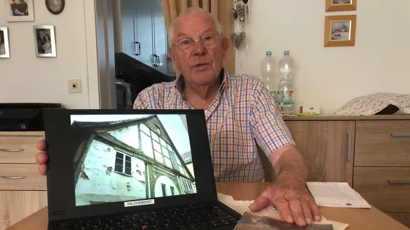 Herbert Wagemann sitzt am K&uuml;chentisch. Auf dem Laptop ist ein Bild der Vorderseite des Hauses an der Schlossstra&szlig;e 19a zu sehen, daneben liegt ein Buch mit seinen Erinnerungen.&nbsp; - &copy; Sven Kienscherf