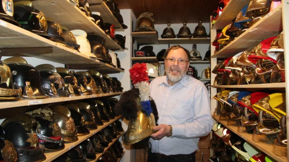 Prall gef&uuml;llte Regale: Umgeben von seinen historischen Feuerwehrhelmen f&uuml;hlt sich Detlef Ullrich pudelwohl. In der Hand h&auml;lt er das &auml;lteste  Exemplar seiner Sammlung, einen franz&ouml;sischen Kommandantenhelm aus dem Jahre 1830. - &copy; Iris Liebig