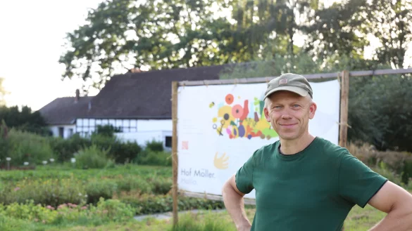 Henning Möller steht vor dem großen Schild, was den Autofahrern signalisieren soll, wo der Hof ist. Direkt daneben ist der Parkplatz. - © Lena Kley